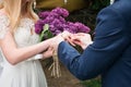 Groom puts wedding ring on brideÃ¢â¬â¢s finger. Bride holding a bouquet from lilac. Bride and groom exchange rings in wedding day. Royalty Free Stock Photo